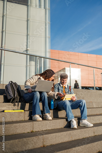 Multiethnic students studying together on campus steps using a laptop and digital tablet