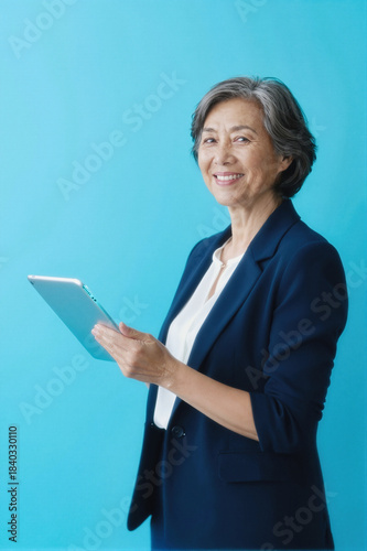 smiling older woman in business suit holding tablet computer against blue background