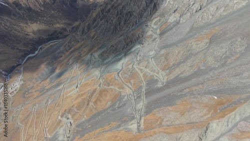 Aerial perspective captures rugged terrain with winding paths and diverse textures, showcasing the natural landscape's intricate details, camera gradually zooms out to reveal more of the scene