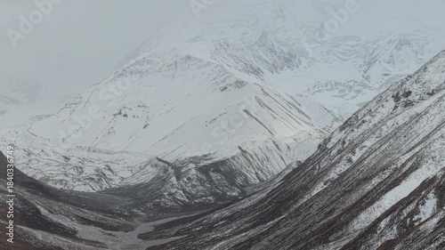 Snow-covered mountains and valleys are captured in a gradual zoom, showcasing the intricate textures of the snow and rocky terrain, enhancing the scene's depth and atmosphere