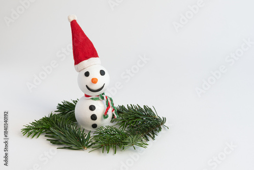 Little handmade snowman with Santa hat and some fir branches around on white background with copy space