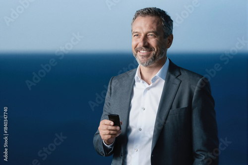 Smiling man in business suit holding smartphone against blue background