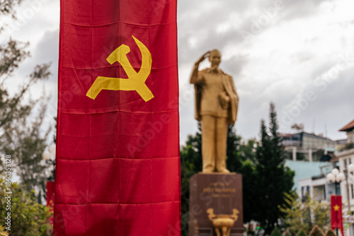 Принти на полотні A communist flag with hammer and sickle displayed in front of a statue of Ho Chi Minh in Vietnam