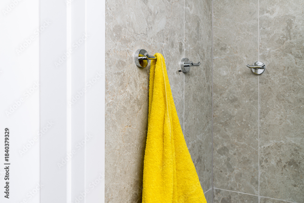 Fototapeta premium Bathroom with gray stone tile walls and chrome towel hooks. a yellow towel is hanging.