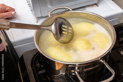 Traditional Lithuanian cepelinai made of potato dough and minced, ground meat inside are cooked in a chrome pot with water.