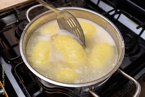 Traditional Lithuanian cepelinai made of potato dough and minced, ground meat inside are cooked in a chrome pot with water.