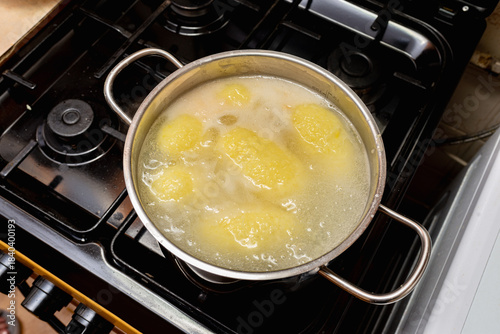 Traditional Lithuanian cepelinai made of potato dough and minced, ground meat inside are cooked in a chrome pot with water.