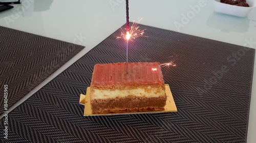 Chocolate puff pastry cake with cream and dulce de leche topping with a sparkler candle.