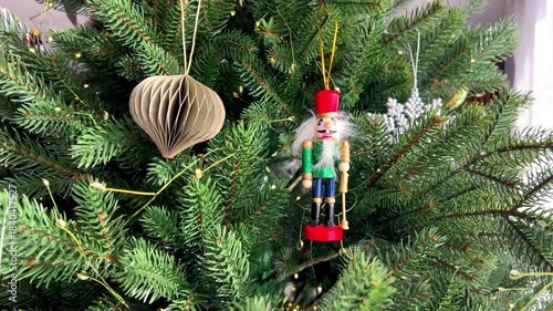 Wooden Nutcracker ornament hanging on a decorated Christmas tree with glowing fairy lights. Traditional holiday decoration, classic Christmas atmosphere, winter celebration and festive seasonal decor