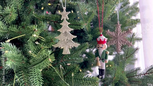  Wooden Nutcracker ornament hanging on a decorated Christmas tree with glowing fairy lights. Traditional holiday decoration, classic Christmas atmosphere, winter celebration and festive seasonal decor