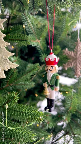  Wooden Nutcracker ornament hanging on a decorated Christmas tree with glowing fairy lights. Traditional holiday decoration, classic Christmas atmosphere, winter celebration and festive seasonal decor