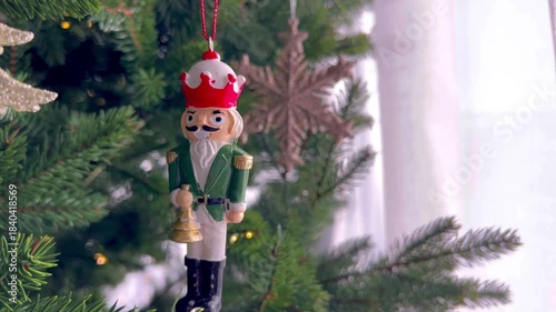  Wooden Nutcracker ornament hanging on a decorated Christmas tree with glowing fairy lights. Traditional holiday decoration, classic Christmas atmosphere, winter celebration and festive seasonal decor