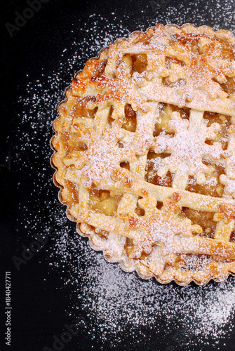 A half of apple pie sprinkled with powdered sugar on black background