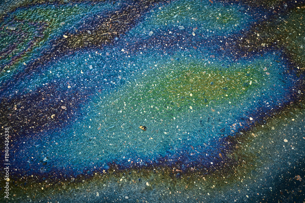 Fototapeta premium Oil Sheen on Pavement Shows Rainbow Colors Near Busy Street During Afternoon