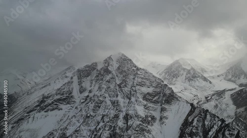 Majestic mountain range features snow-covered peaks and dramatic clouds, as the camera pans across the breathtaking landscape, revealing the rugged terrain and serene atmosphere