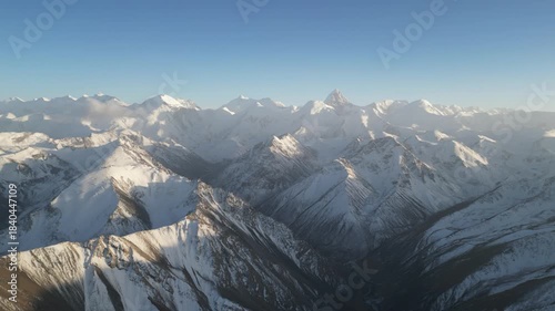 Snow-capped mountain range panorama showcases majestic peaks and valleys, with a gradual zoom out revealing the expansive landscape and clear blue sky, highlighting natural beauty and serenity