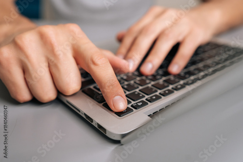 Hand pressing laptop power button in close-up, starting up portable computer on desk to begin work, study or everyday productivity in modern home or office setting.
