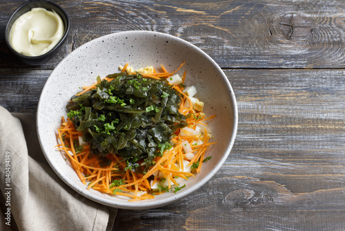 Seaweed salad ingredients with carrots, chopped eggs and diced onions in ceramic bowl on rustic wooden table