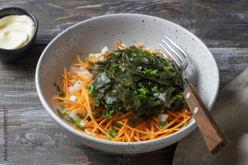 Seaweed salad ingredients with carrots, chopped eggs and diced onions in ceramic bowl on rustic wooden table