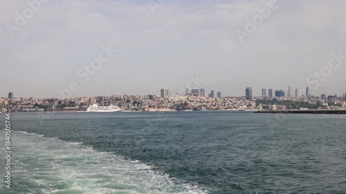 View of Istanbul's urban landscape across the water, featuring modern skyscrapers and a cruise ship.