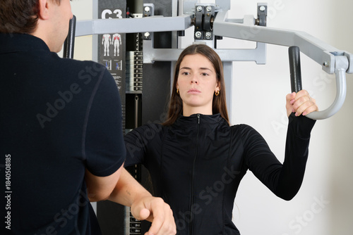 Young adult woman focusing on chest press exercise with the guidance of a male personal trainer in a gym setting