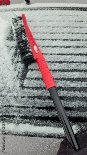 closeup of a person removing snow from the back window of a vehicle during a weather event.