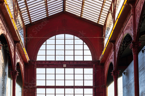 Large interior hall with red iron arches and expansive window wall illuminated by soft daylight, Portugal, Porto, 11 October 2025