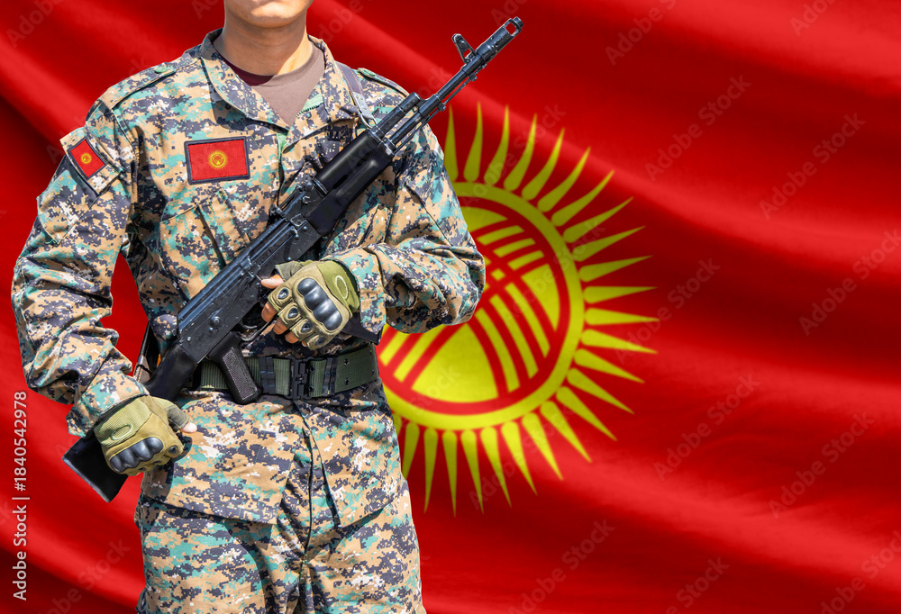 Obraz premium Kyrgyzstan flag with soldier in military uniform holding assault rifle in front of it