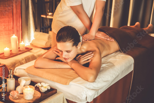 Caucasian woman customer enjoying relaxing anti-stress spa massage and pampering with beauty skin recreation leisure in warm candle lighting ambient salon spa at luxury resort or hotel. Quiescent