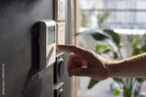 Hand adjusting temperature on smart home thermostat, smart home temperature control panel being operated, indoor climate