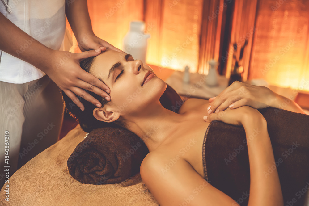 Fototapeta premium Caucasian woman enjoying relaxing anti-stress head massage and pampering facial beauty skin recreation leisure in warm candle lighting ambient salon spa in luxury resort or hotel. Quiescent