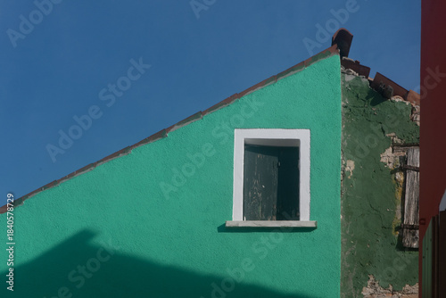 Dettaglio del tetto di una casa dipinta di verde di Burano con una finestra dalla cornice bianca