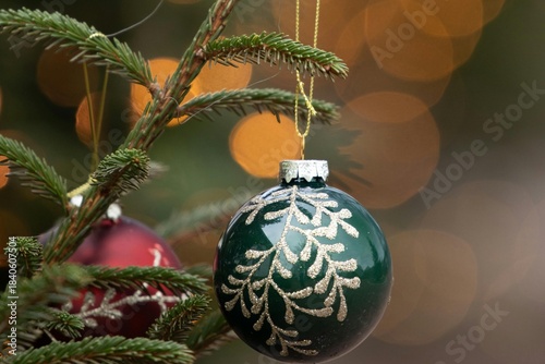 Close-up of a festive gold glass Christmas ball ornament hanging on a green fir tree branch for the holiday season decoration