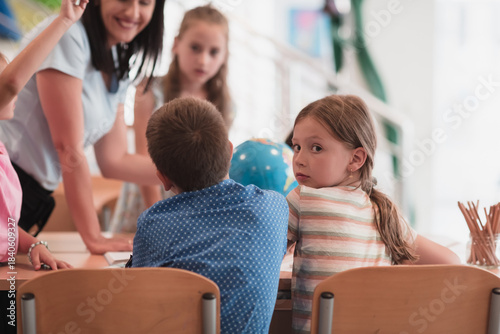 Female teacher with kids in geography class looking at globe. Side view of group of diverse happy school kids with globe in classroom at school.