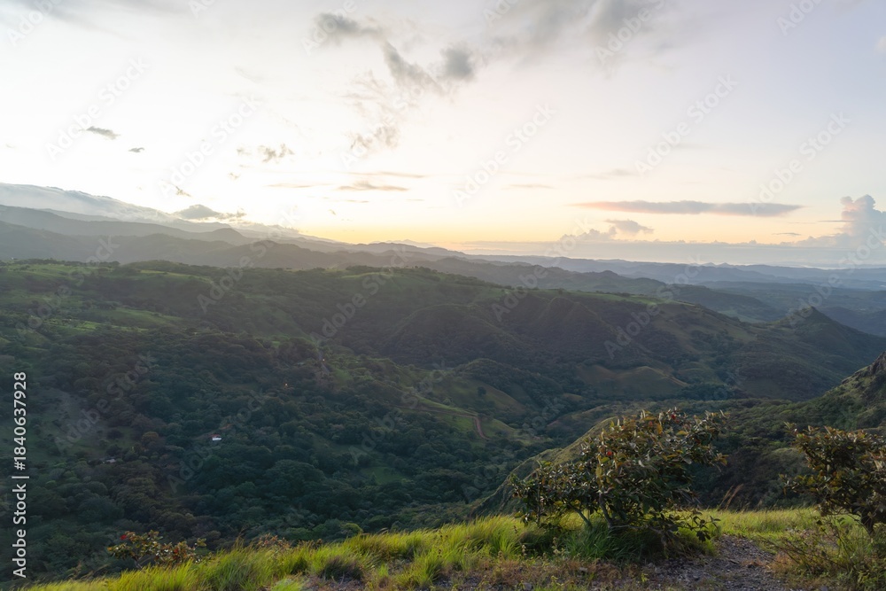 Naklejka premium Foreground Grass and Shrubs Framing a Panoramic Sunset over Tropical Hills