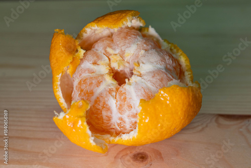 Fresh orange fruit, partially peeled, revealing juicy segments inside, placed on a wooden surface, showcasing vibrant colors and natural textures in a healthy food concept