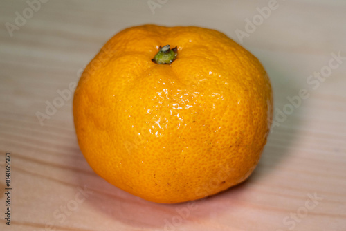 Bright orange citrus fruit with textured skin and green stem resting on a light wooden surface, showcasing freshness and natural beauty in a simple composition