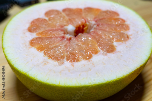 Freshly cut grapefruit half showcasing vibrant pink flesh and juicy segments, resting on a wooden surface, highlighting the natural textures and colors of the fruit