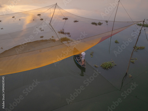 Aerial view of a lone fisherman casts his net in the tranquil waters of the river, the golden light painting the scene in warm hues, Hoi An, Quang Nam, Vietnam.