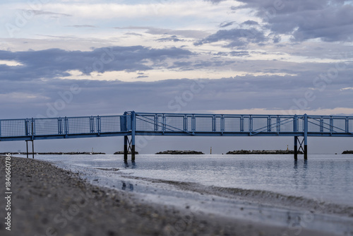 Fototapeta Naklejka Na Ścianę i Meble -  A pier stretching from the beach into the sea like a bridge to the horizon, Adriatic coast near Rimini, Italy, calm atmosphere with soft daylight.