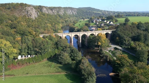 Drone shot of the impressive stone viaduct in Clécy, Normandy, overlooking the Orne River. 4K video with side-view motion. The bridge, framed by autumn trees, creates a picturesque landscape.