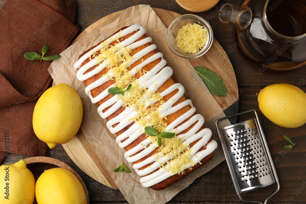 Fototapeta premium Tasty lemon cake decorated with icing, zest and mint served on wooden table, flat lay