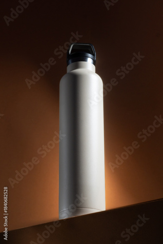 Botella térmica blanca sobre fondo oscuro con luz cálida de estudio