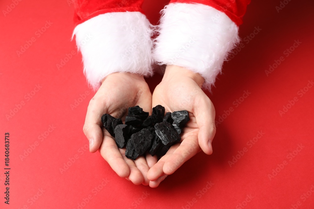 Fototapeta premium Christmas gift for naughty kids. Santa Claus with pieces of black coal on red background, above view