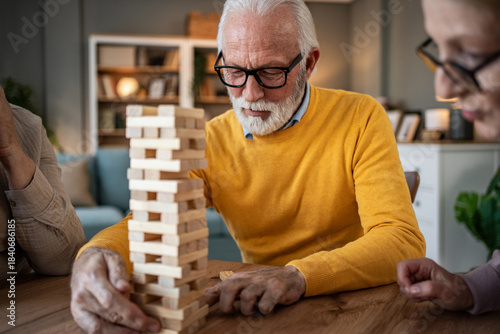 Senior man concentrating on playing jenga game with friends