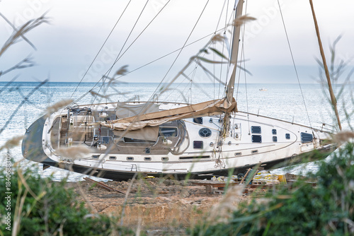 Javea Alicante 10 12 2025 – A stranded sailboat resting on the rocky coastline of Javea, Spain, with clear Mediterranean waters and dramatic shore scenery.