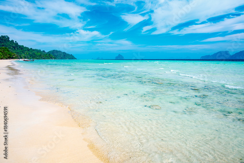 Koh Kradan beach with translucent turquoise water lapping soft sand, lush green isles and a distant traditional longtail boat serene tropical escape and untouched paradise
