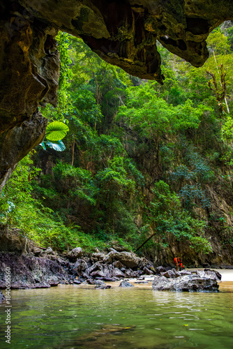 Emerald Cave entrance showing vibrant green water meeting a rocky shore and dense tropical jungle foliage, highlighting the natural beauty of Koh Mook island