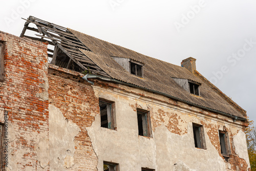 Фотография Exterior of an old, abandoned, and derelict brick and stucco building with a partially collapsed slate roof and crumbling walls against a white sky, symbolizing decay and abandonment