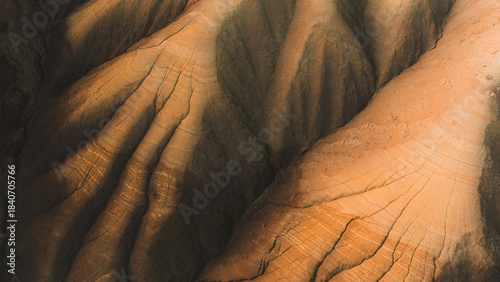 Aerial view of an arid landscape sculpted by erosion, where sunlight paints the ridges in warm hues, contrasting with the shadows in the deep ravines, Centuripe, Sicilia, Italy.